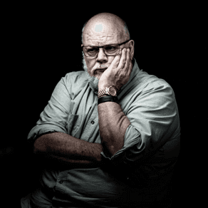 Person wearing a grey shirt and a watch, with arms crossed, in a dark setting.