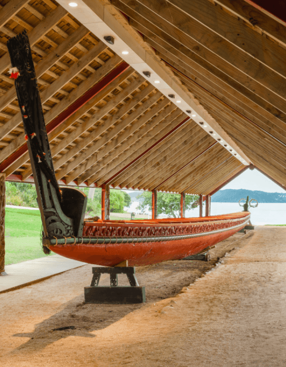 A traditional wooden carved canoe displayed under a wooden shelter near a body of water.