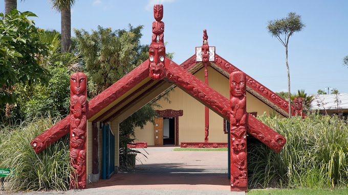 Entrance to a traditional building with ornate red carvings and surrounded by lush greenery.