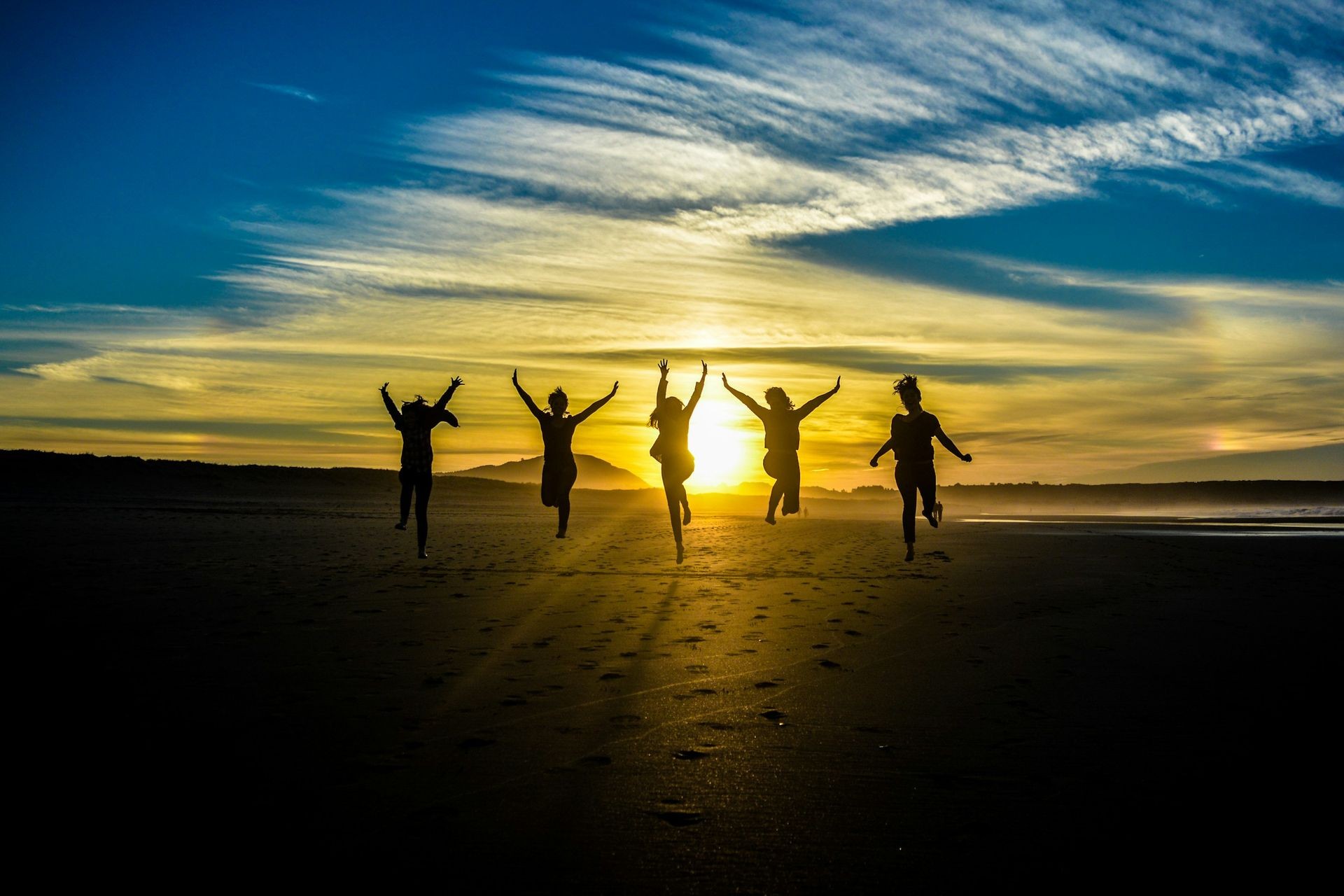 Silhouette of five people jumping on the beach during sunset with a colorful sky in the background.