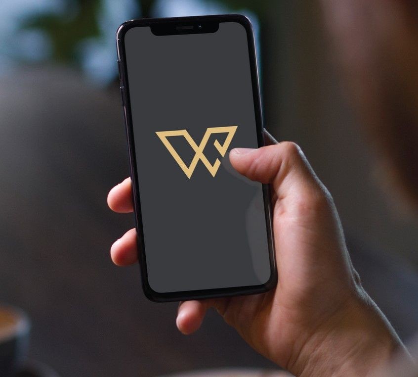 Close-up of a hand holding a smartphone displaying a gold geometric logo on a dark screen.